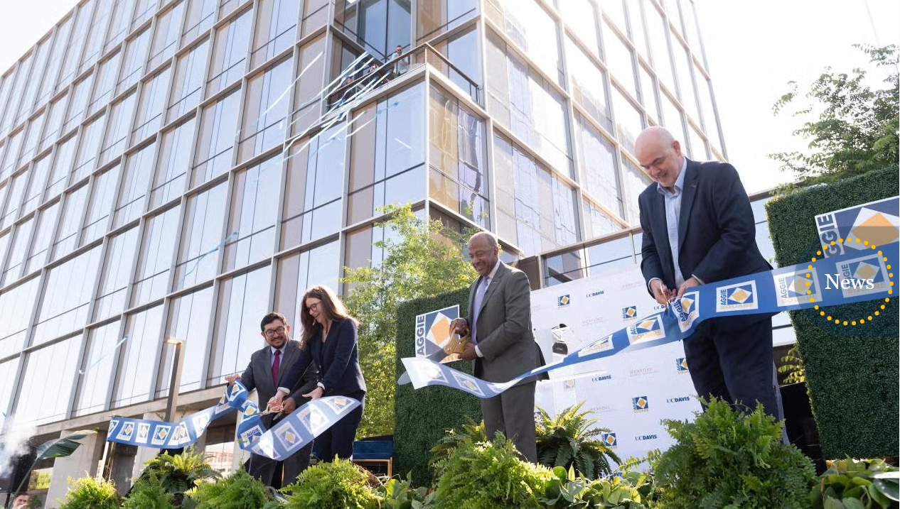Four people participate in a ribbon cutting ceremony with a modern glass-walled building in the background.