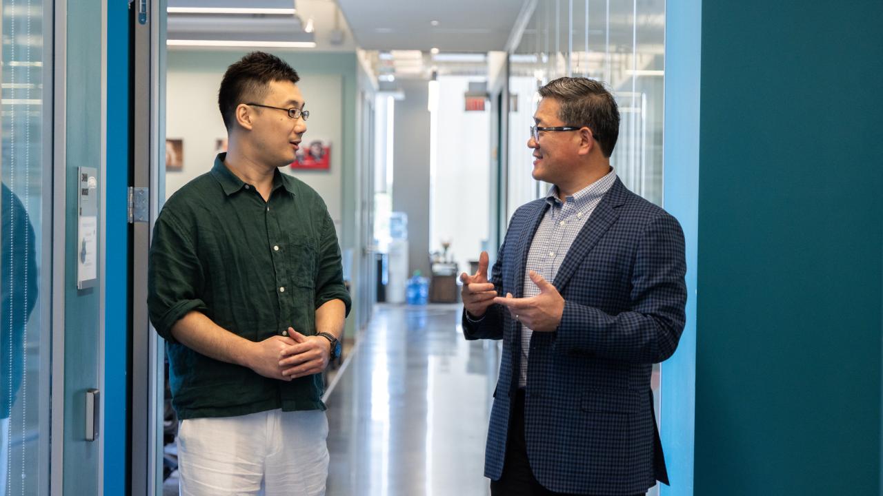 Two men talk in office hallway.