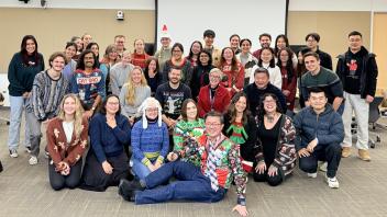 Group of people gathers for a photo. Many of them are wearing holiday sweaters.