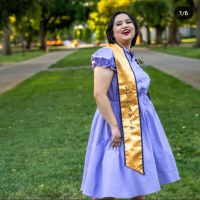 A young woman with short black hair smiles with her chin up. She is wearing a lavender dress and a UC Davis graduation stole.
